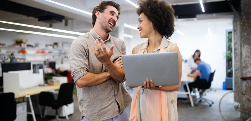 A man and a woman looking at a computer in a busy workplace.