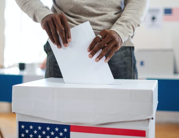 A man putting a paper ballot into a ballot box on election day.