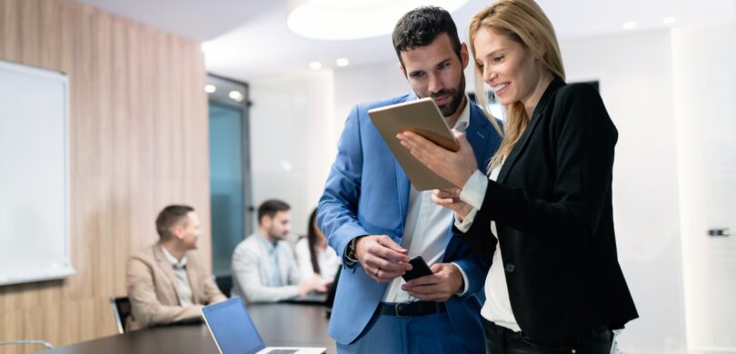 A man and a woman in a business meeting, looking at a tablet together.