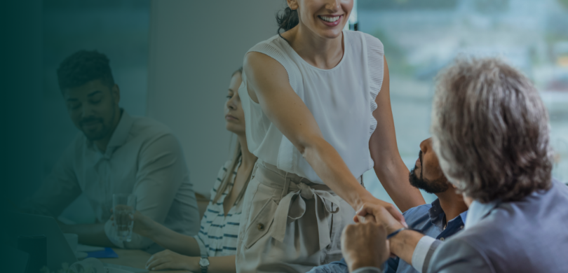 A young woman and older man shaking hands in a professional setting.