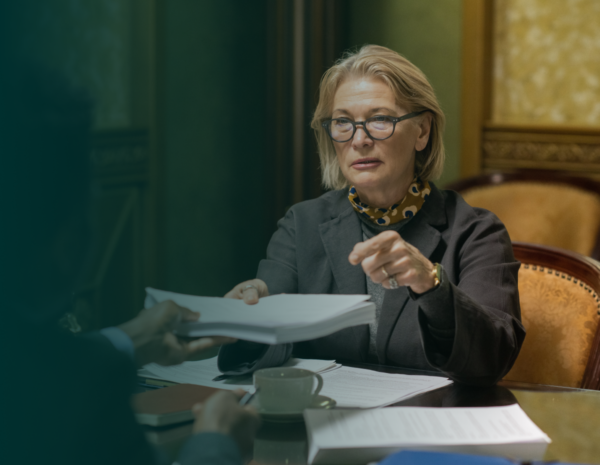 A woman sits in a business meeting surrounded by papers.